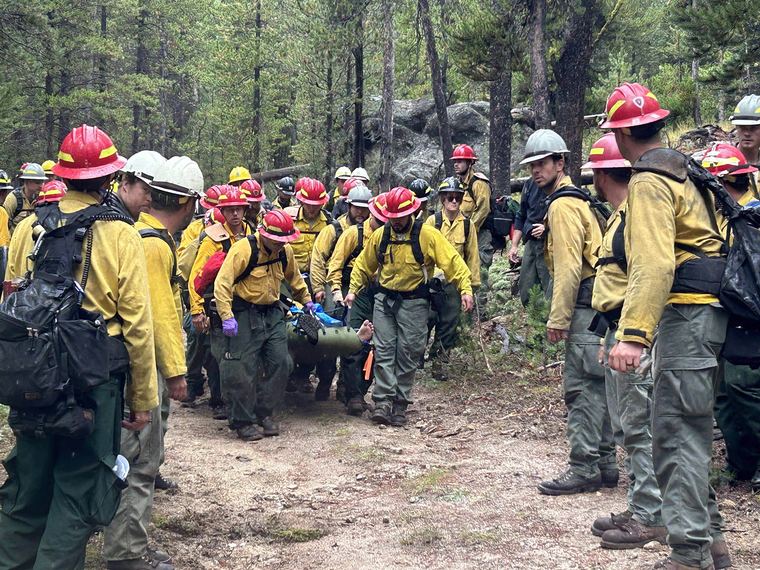 Wildland fire crews carry a patient in a litter along a forest road