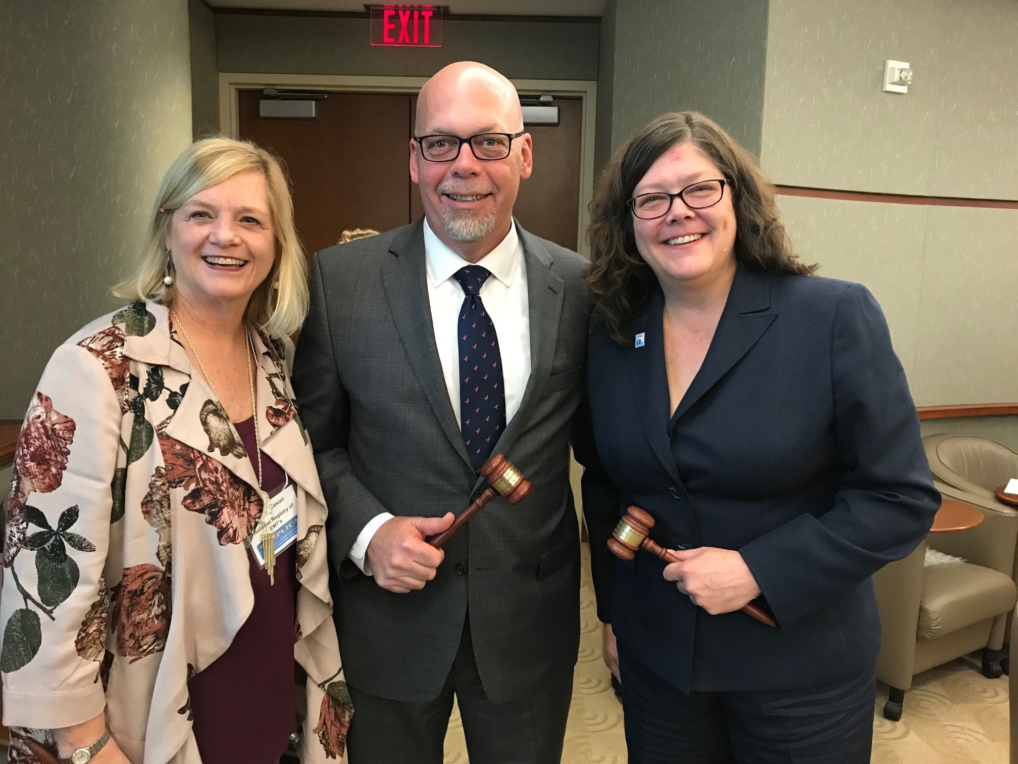 The three inaugural honorary commissioners standing together, two holding gavels, at the first meeting of the Interstate Commission for EMS Personnel Practice.